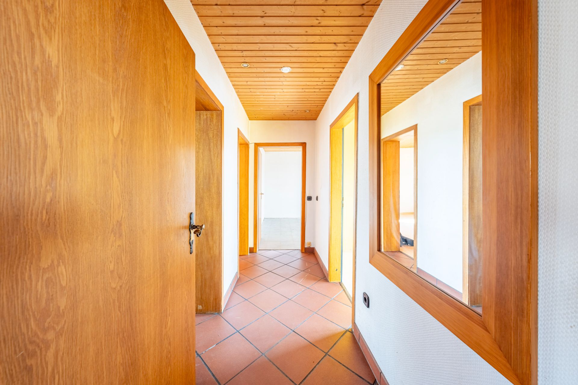 Heller Flur mit Holztüren, gefliestem Boden und großer Wandspiegel.