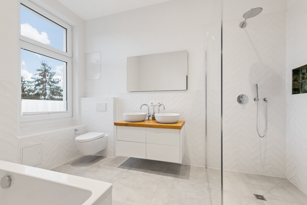 Helles, modernes Badezimmer mit Dusche, Doppelwaschbecken, WC und großer Fensterfront.