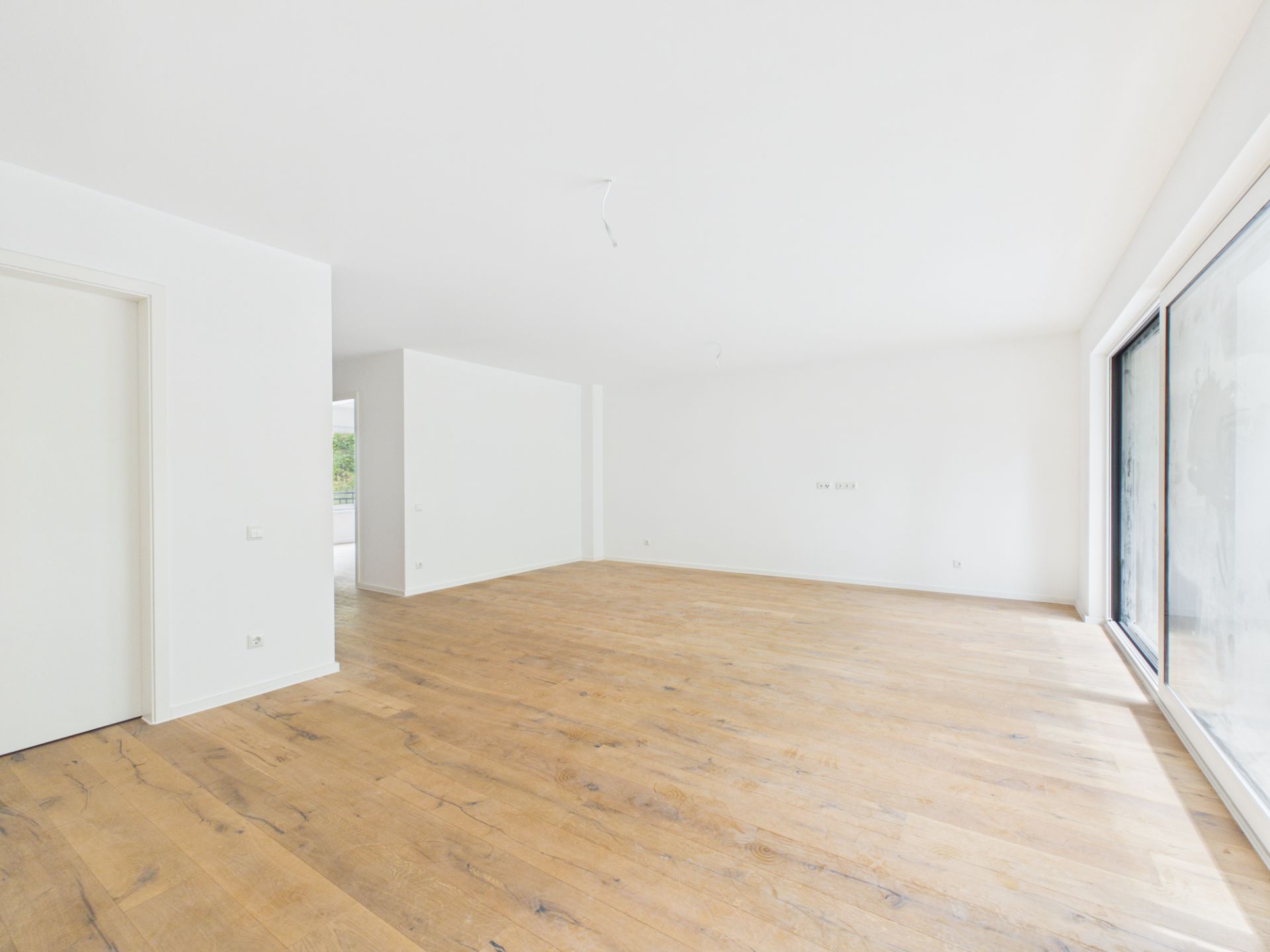 Heller, leerer Raum mit Holzboden und großer Fensterfront.
