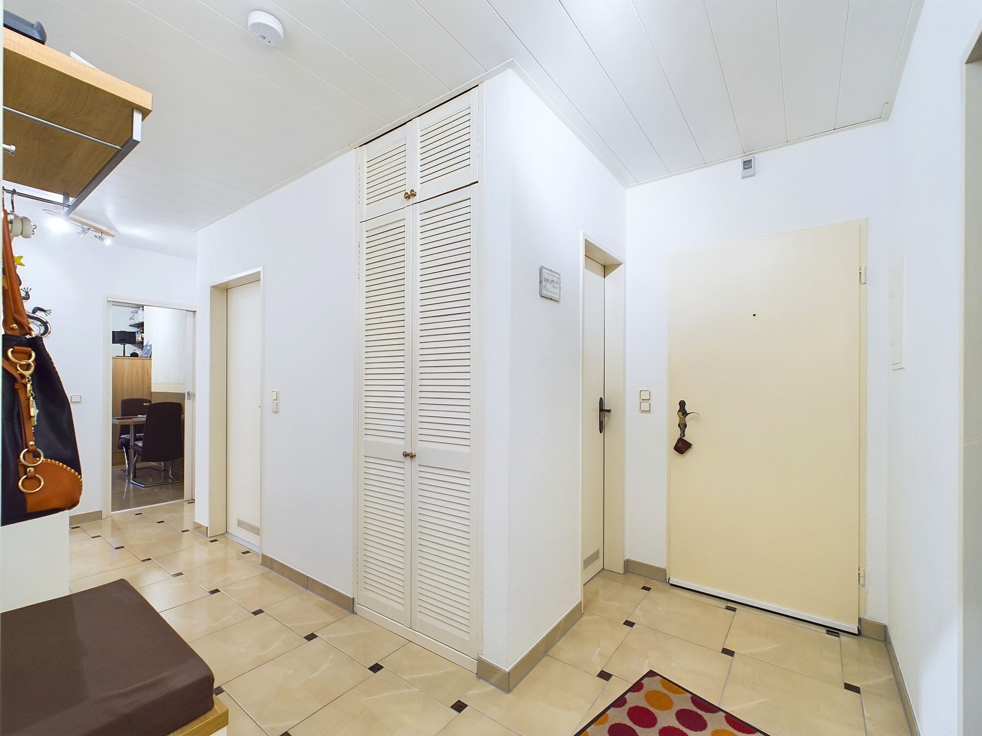 Heller Flur mit Fliesenboden, weißem Wandschrank und Eingangstür.