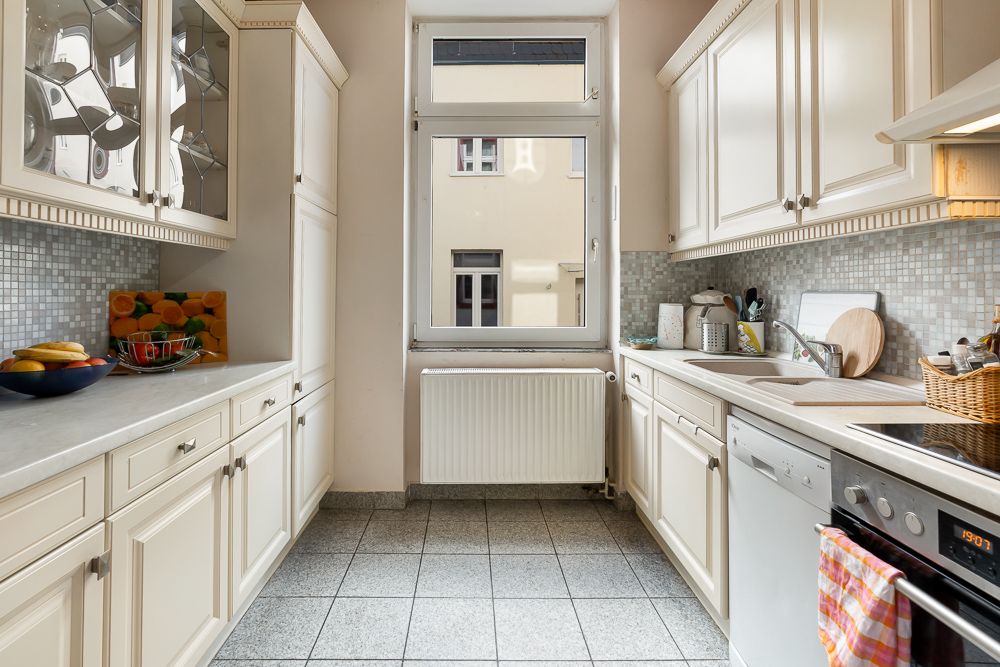 Helle Küche mit weißen Schränken, großem Fenster und Fliesenboden.