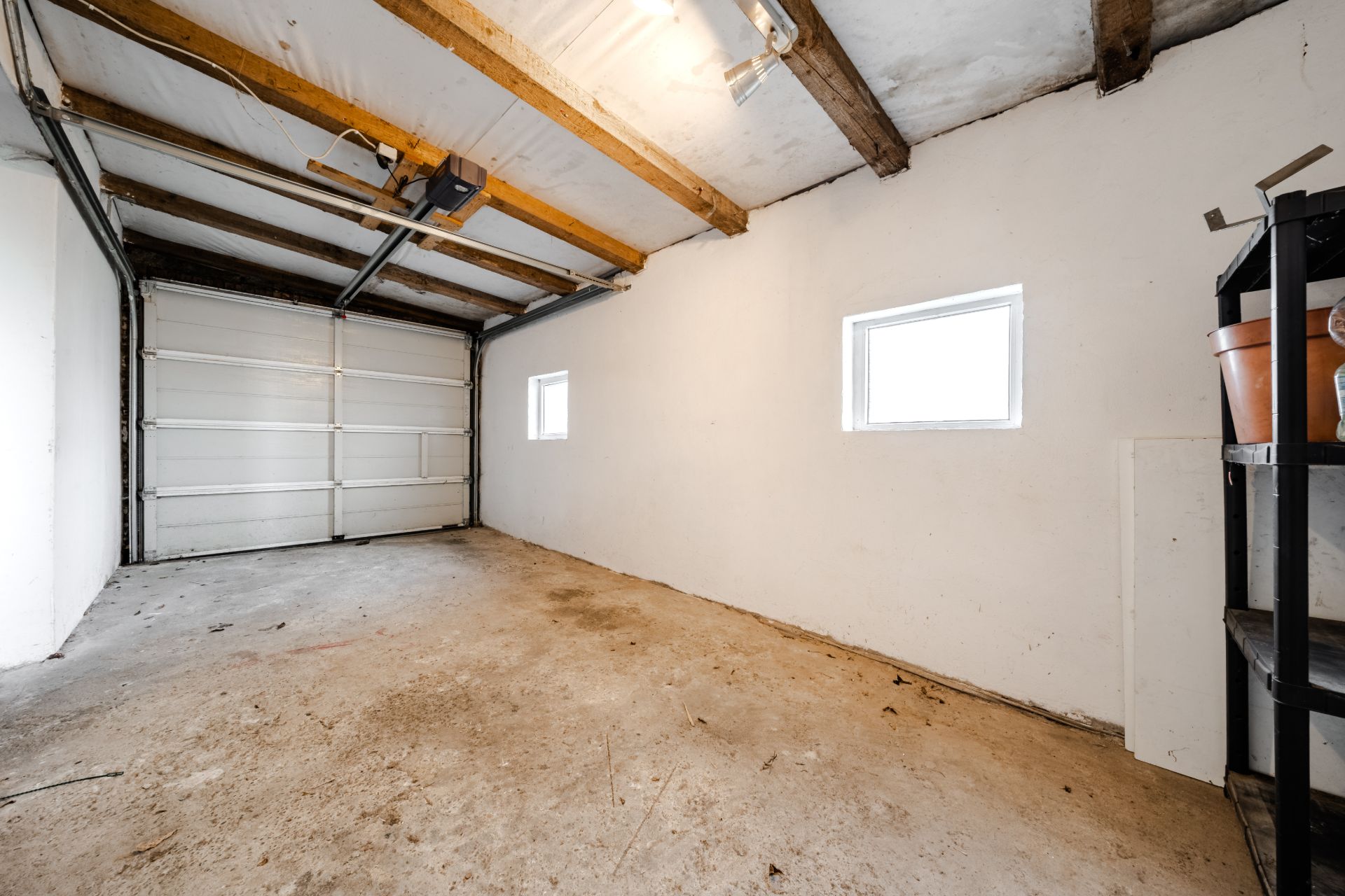 Leere Garage mit zwei Fenstern, Regalen und sichtbaren Holzbalken an der Decke.
