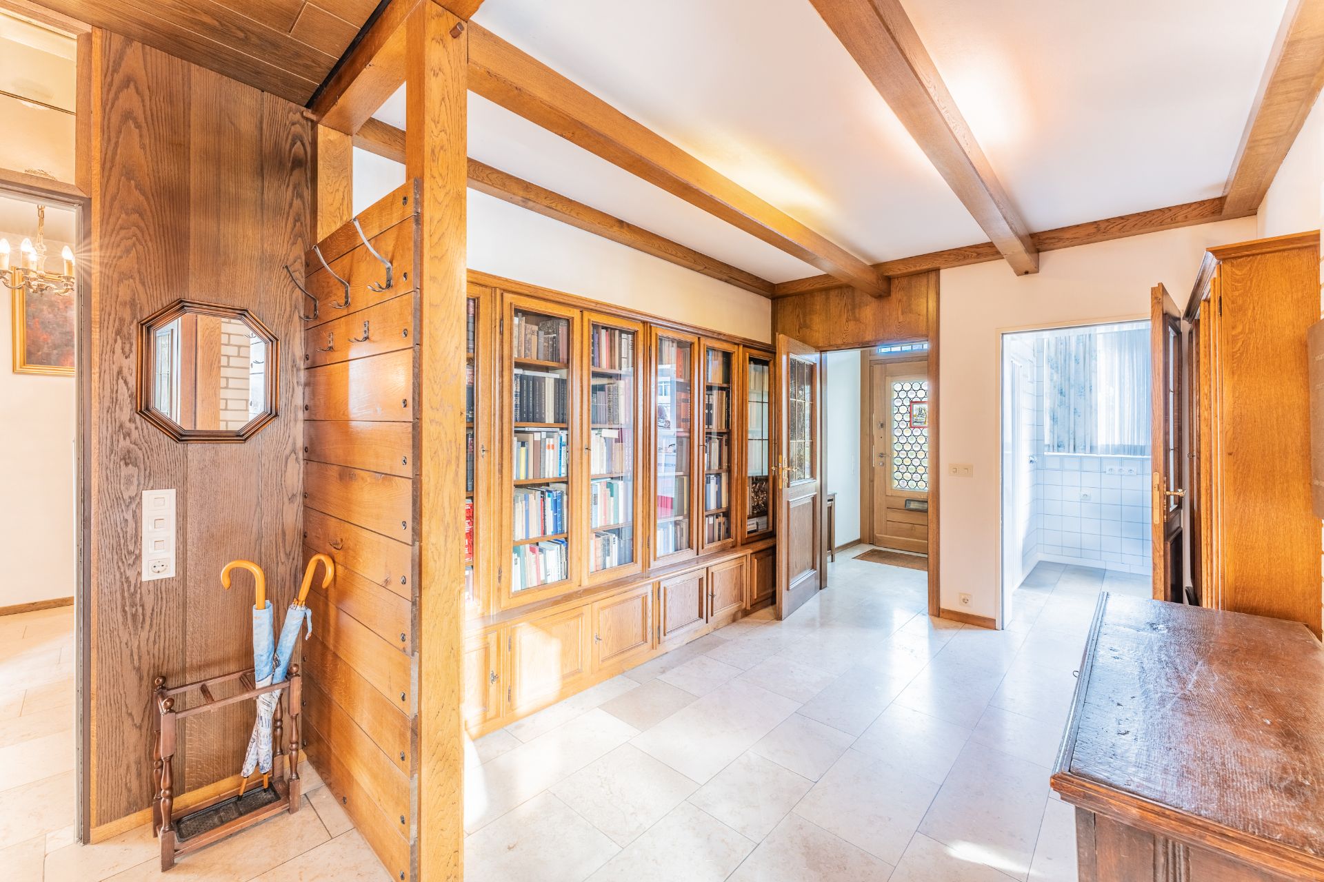 Heller Flur mit Holzdecke, Bücherregal, Garderobe, Spiegel und zwei Regenschirmen.