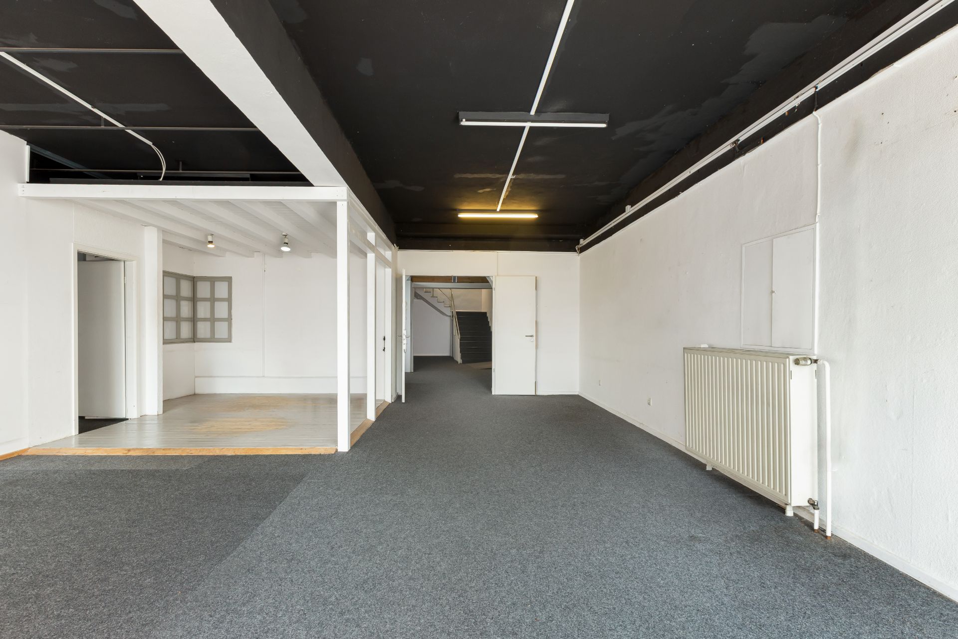 Großer, leerer Raum mit dunkler Decke, grauem Teppich und Heizkörper an der Wand.