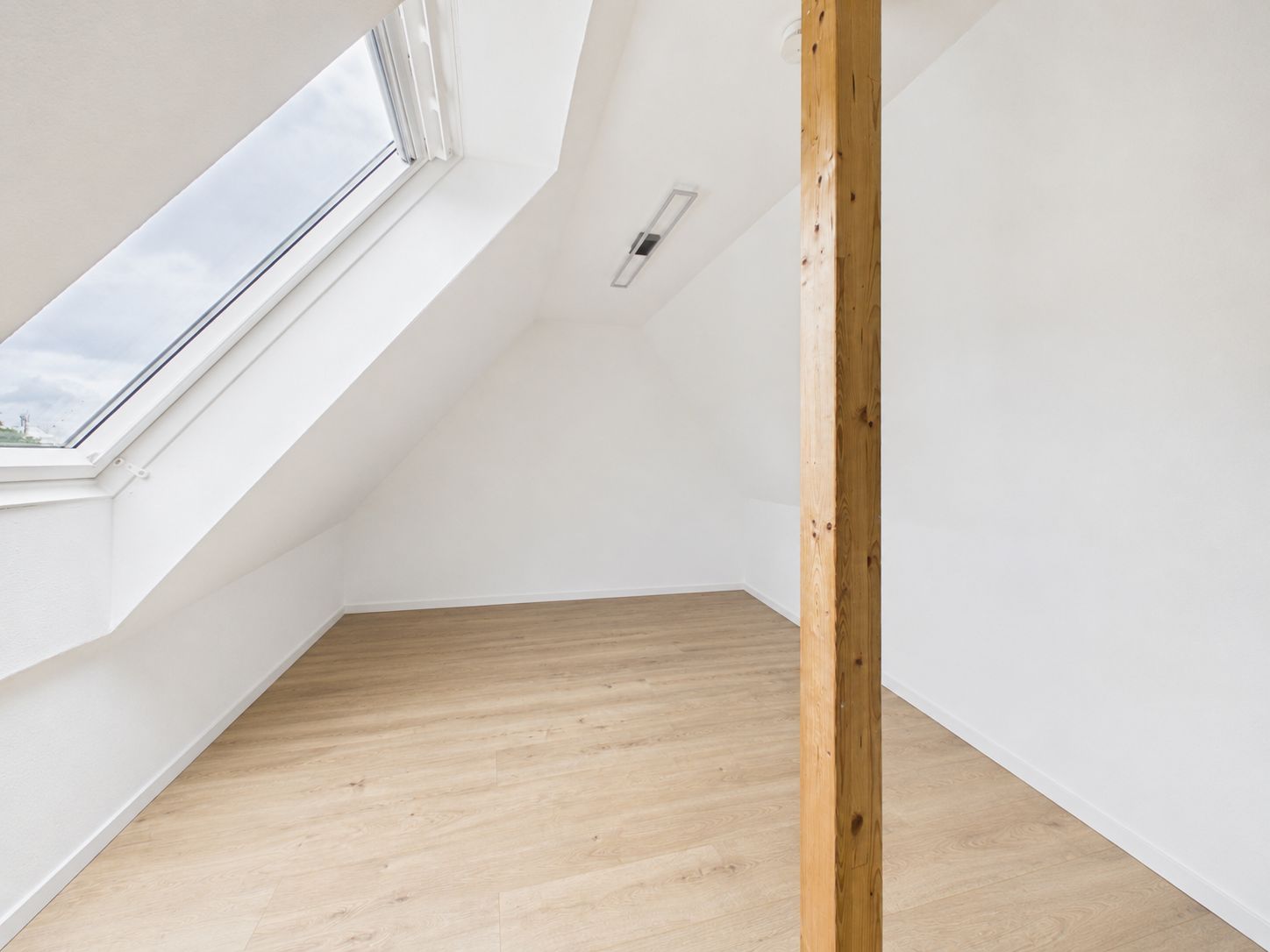 Heller Dachraum mit Holzsäule, großem Dachfenster und hellem Holzfußboden.