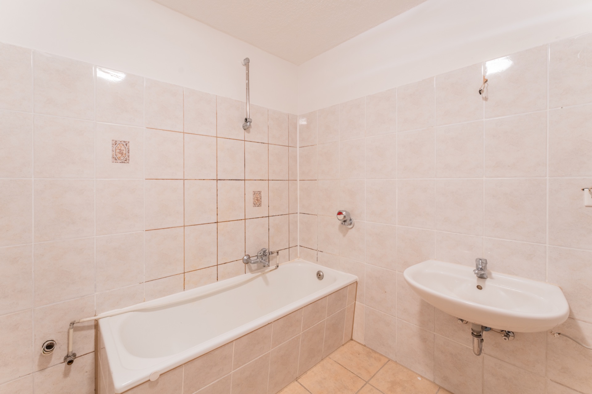 Gefliestes Badezimmer mit Badewanne und Waschbecken, helle Wand- und Bodenfliesen.