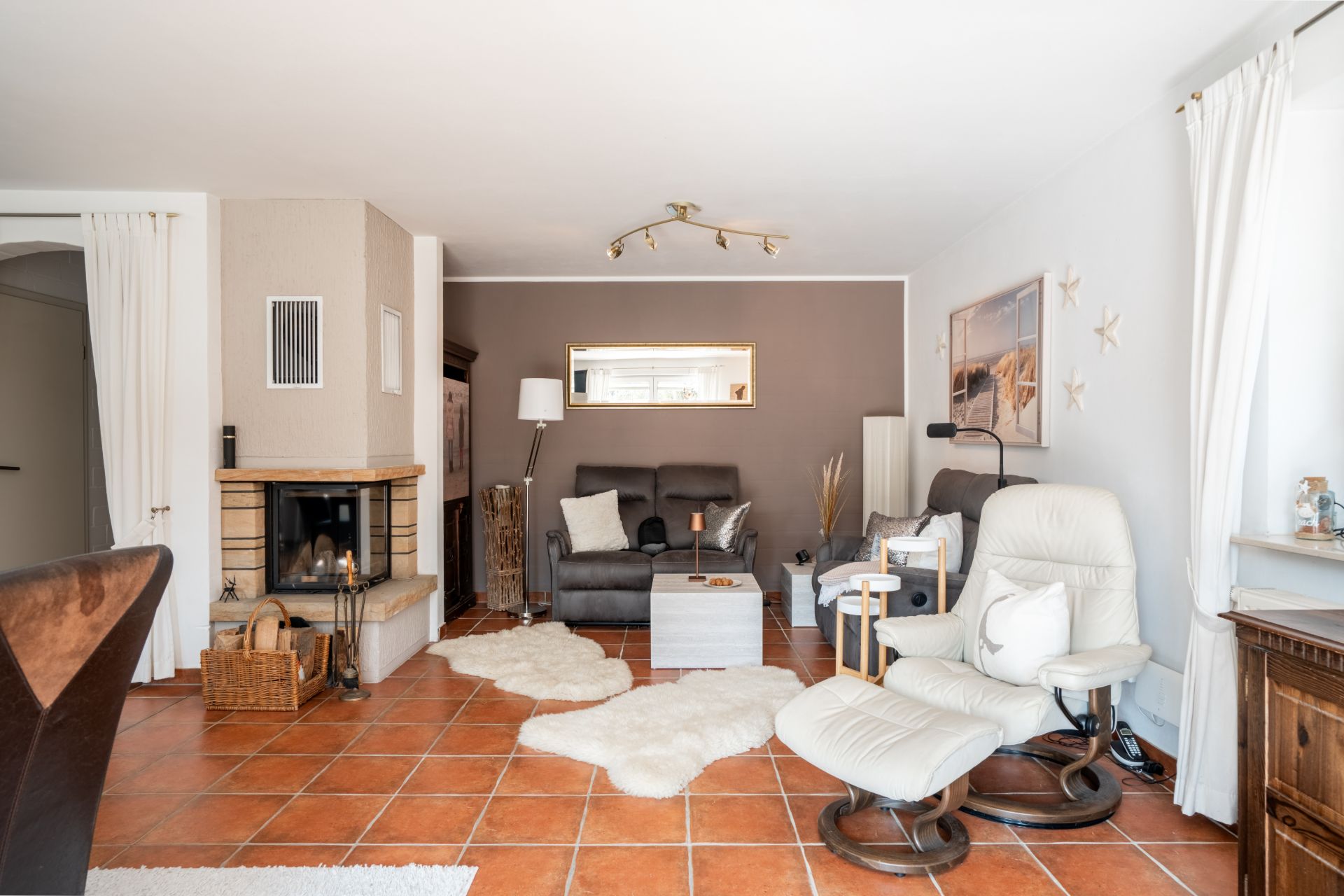 Wohnzimmer mit Kamin, Sesseln, Sofa, Fliesenboden und Dekorationen.