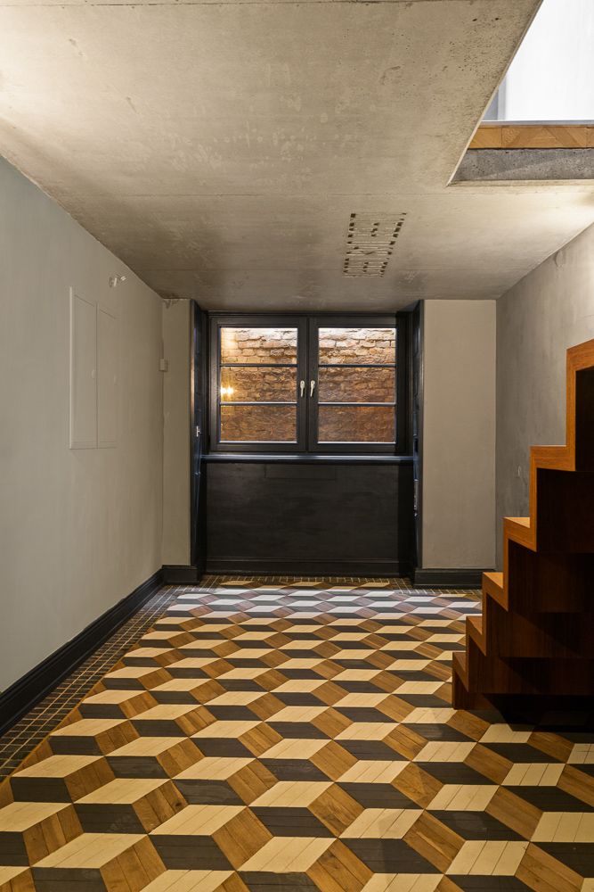 Flur mit gemustertem Holzboden, Treppe rechts und Fenster mit Blick auf eine Ziegelwand.