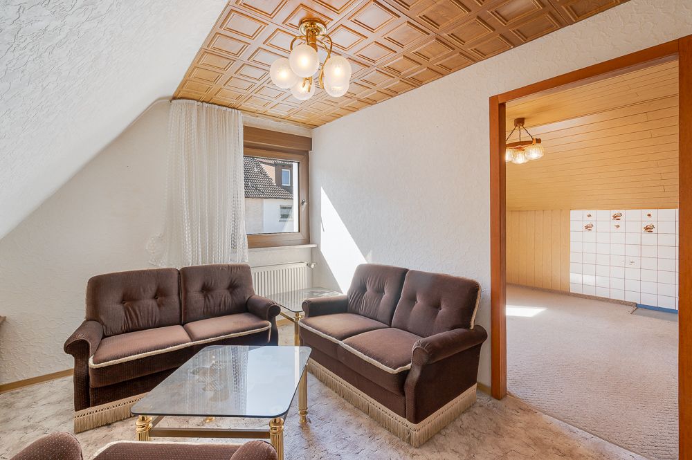 Wohnzimmer mit braunen Sofas, Glastisch, Holzdecke und Blick in ein weiteres Zimmer.