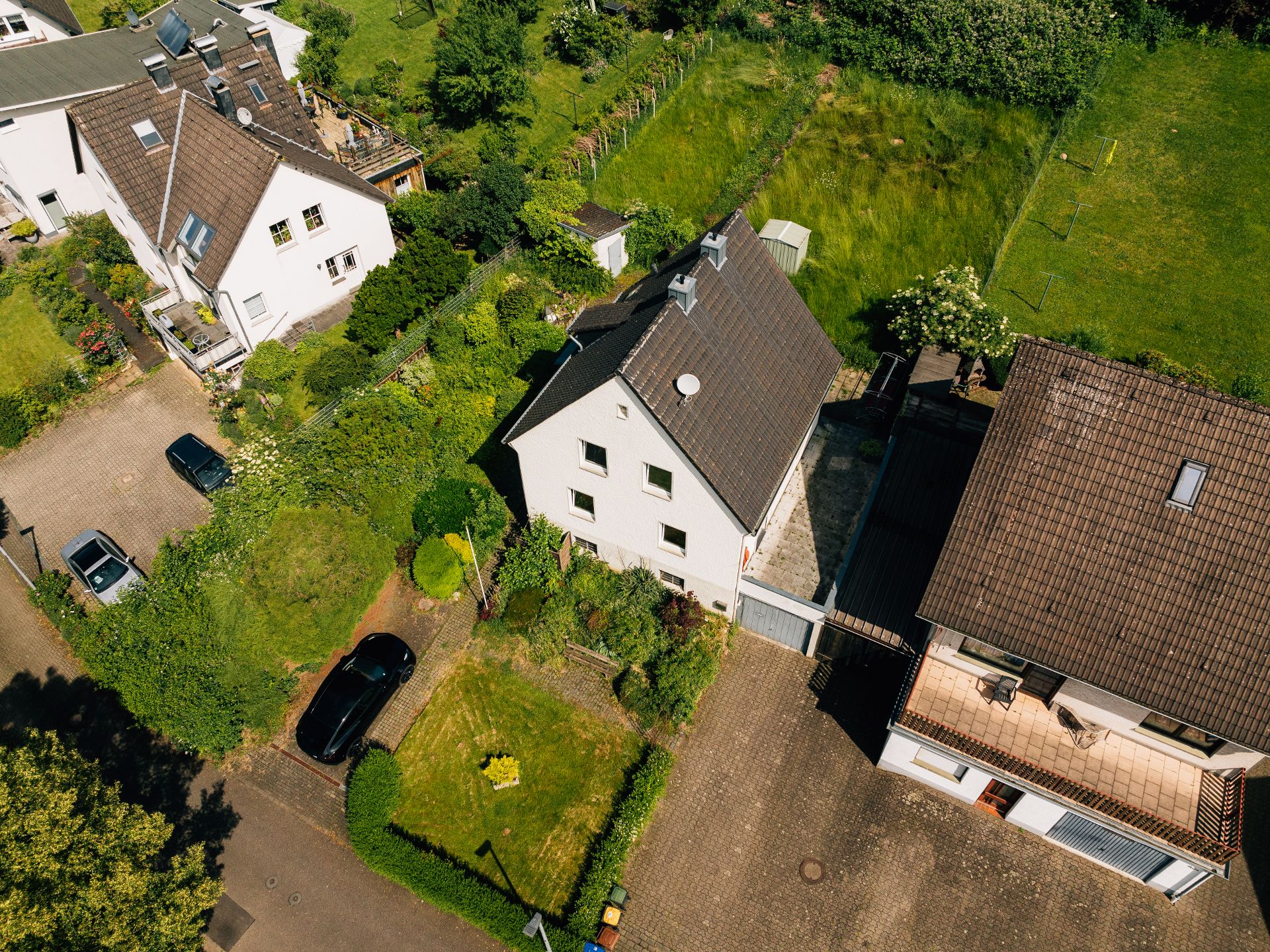 Luftaufnahme von Wohnhäusern mit Garten, Auffahrt und parkenden Autos.