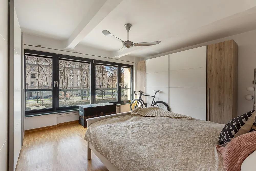Helles Schlafzimmer mit großem Fenster, Doppelbett, Kleiderschrank und einem Fahrrad in der Ecke.