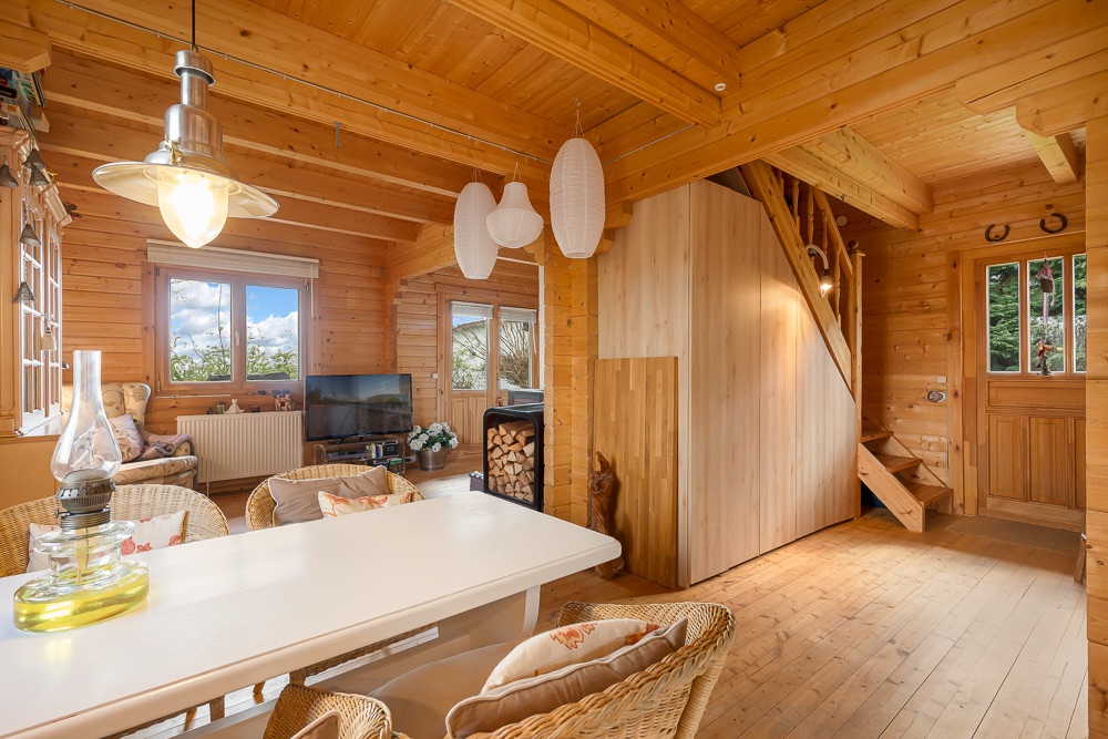 Helles Wohnzimmer aus Holz mit Esstisch, Korbstühlen, Treppe und Fenster.