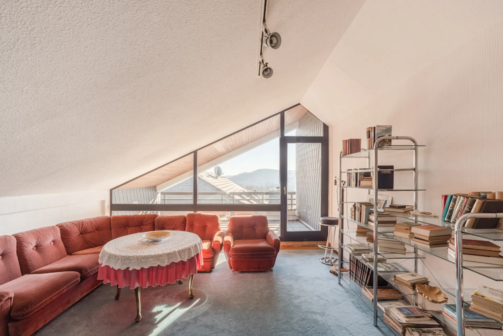 Wohnzimmer mit roten Sofas, rundem Tisch und Regal voller Bücher unter einer Dachschräge.