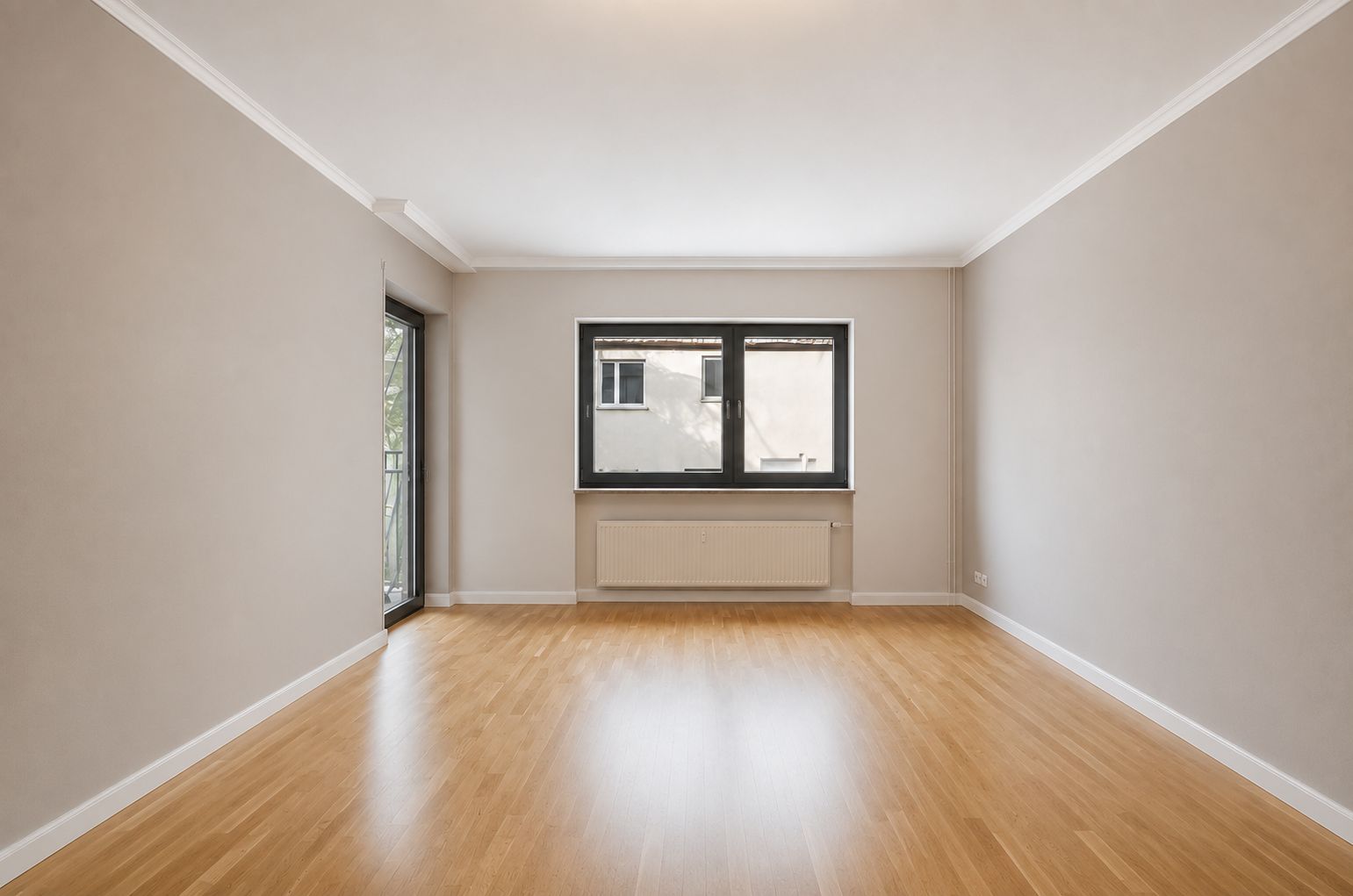 Leerer Raum mit Holzfußboden, Fenster und Tür zu einem Balkon, helle Wände.