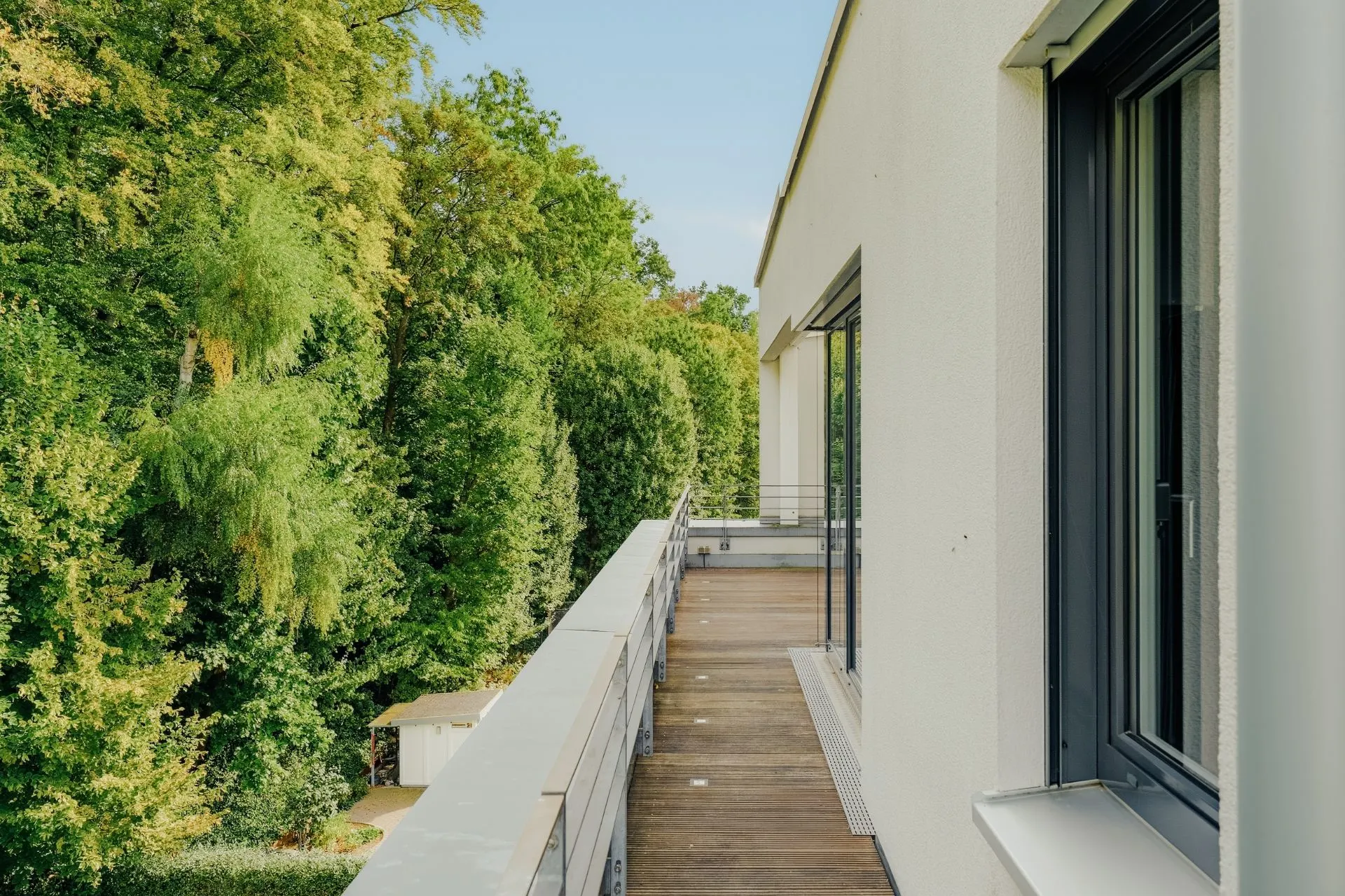 Balkon mit Holzboden an einem modernen Wohnhaus, mit Blick auf grüne Bäume.