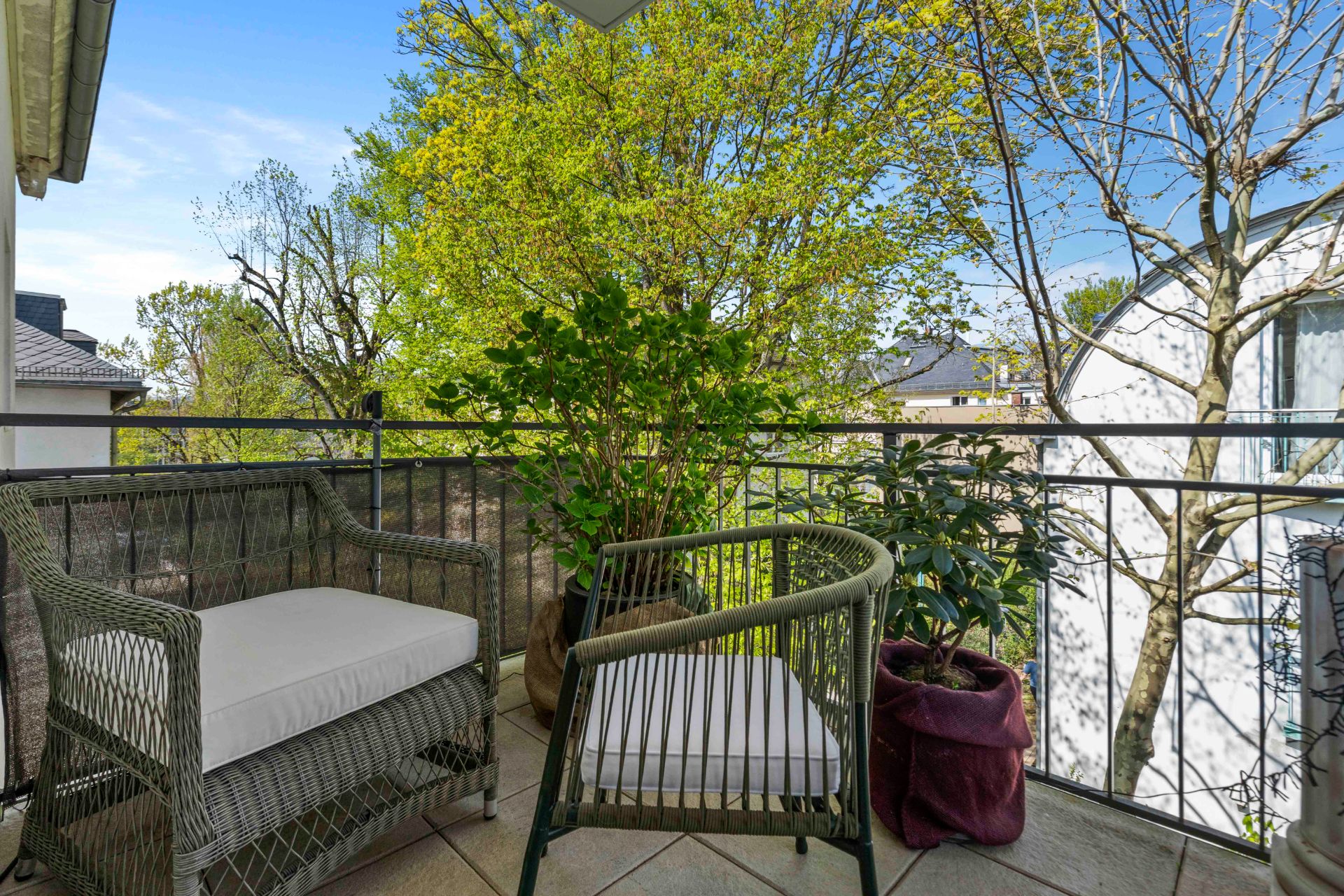 Balkon mit zwei Polsterstühlen, Pflanzen und Blick auf Bäume.