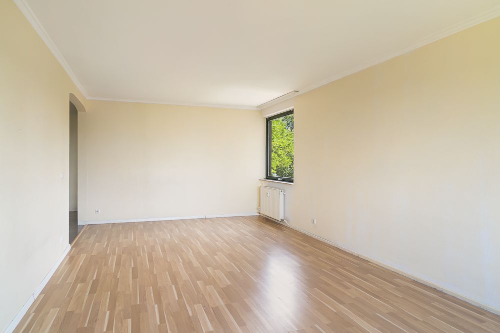 Leeres Zimmer mit hellem Holzboden, cremefarbenen Wänden und großem Fenster.
