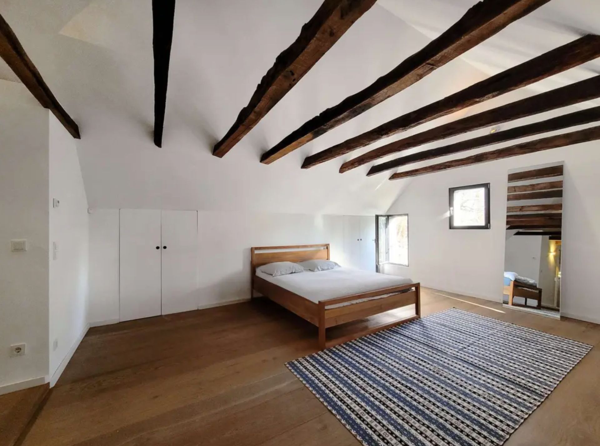 Schlafzimmer mit Holzbalkendecke, Doppelbett und Teppich auf Holzboden.