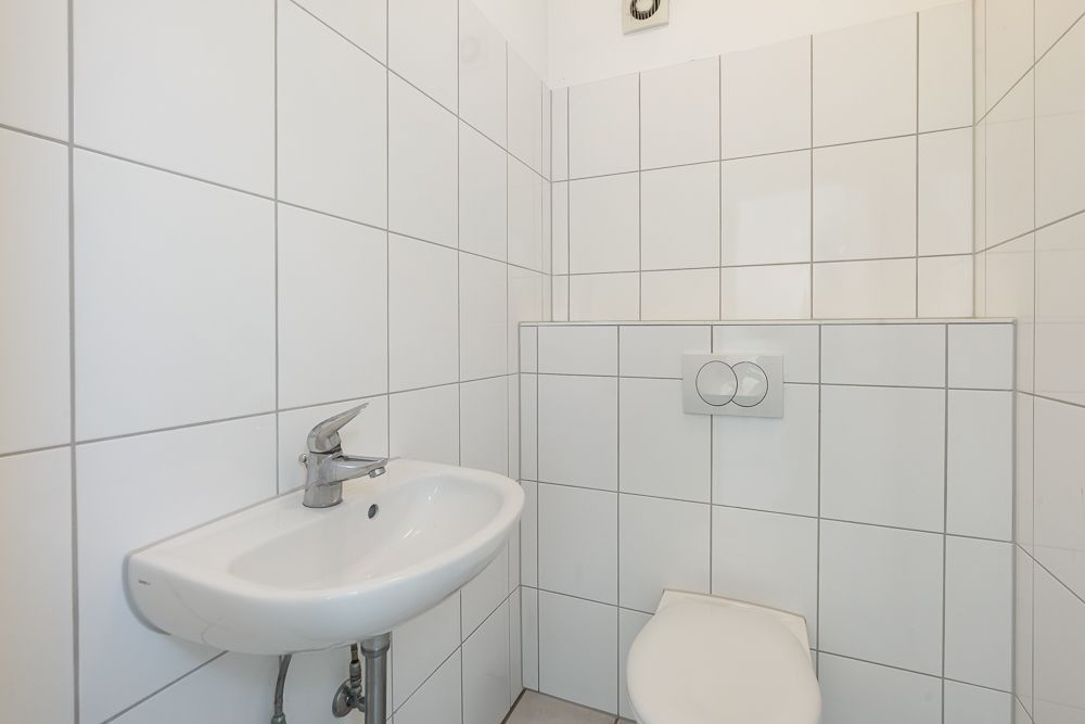 Kleines Badezimmer mit WC und Wandwaschbecken, weiße Fliesen an den Wänden.