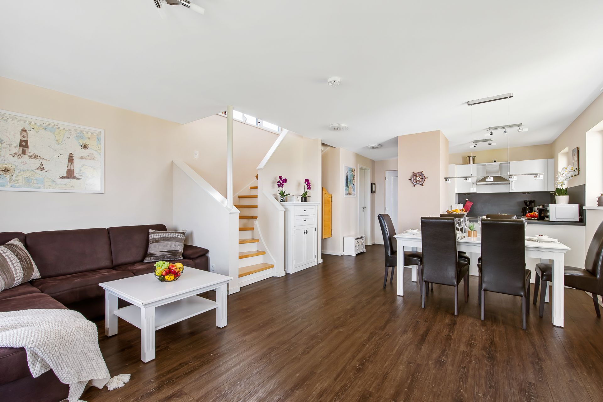 Helles Wohnzimmer mit braunem Sofa, Esstisch, offener Küche und Treppe.