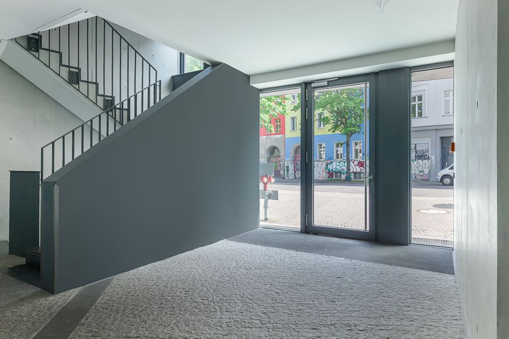 Heller Eingangsbereich mit Treppe und großer Glastür, Blick auf die Straße mit bunt bemalten Häusern.