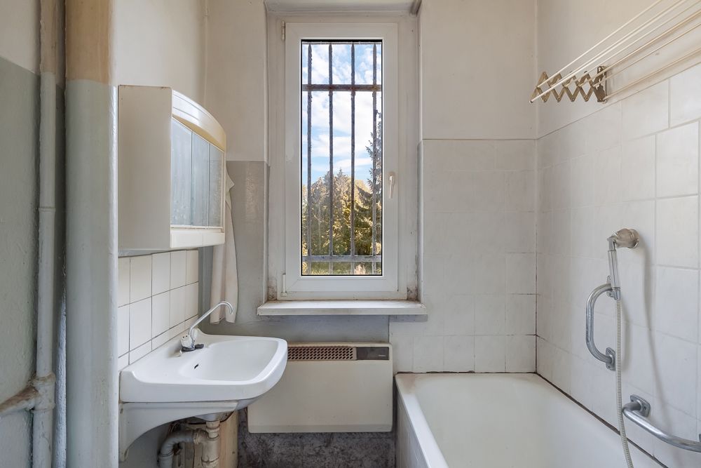 Kleines Badezimmer mit Waschbecken, Badewanne und einem Fenster mit Gitter.