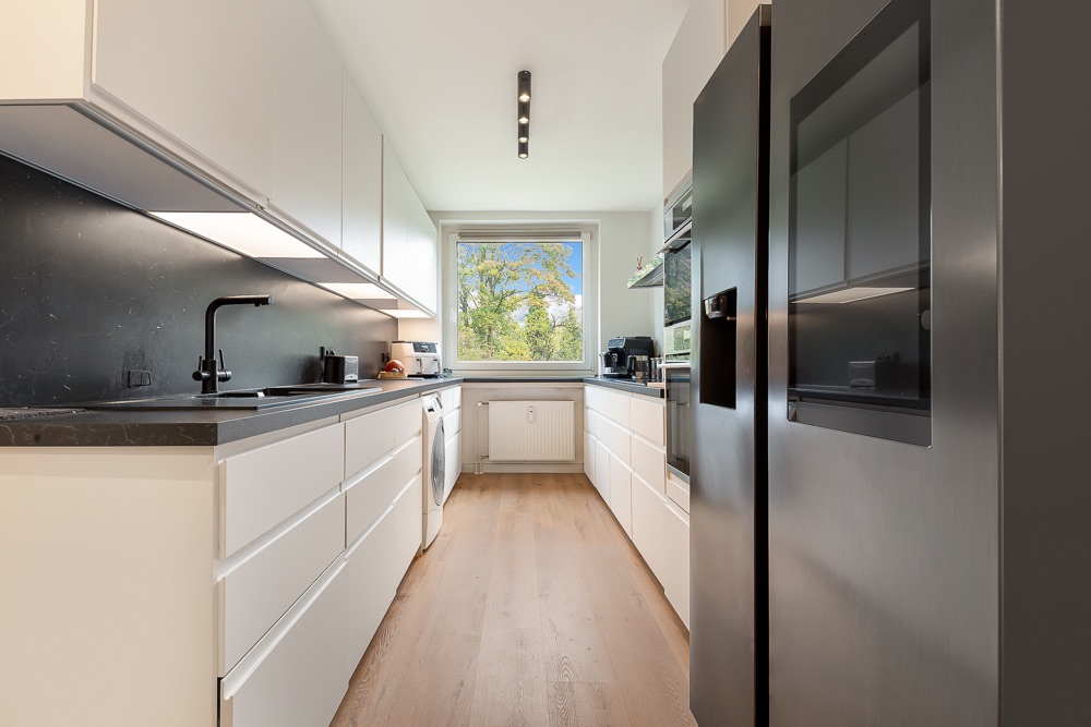 Moderne helle Küche mit weißen Schränken, schwarzer Arbeitsplatte und großem Fenster.