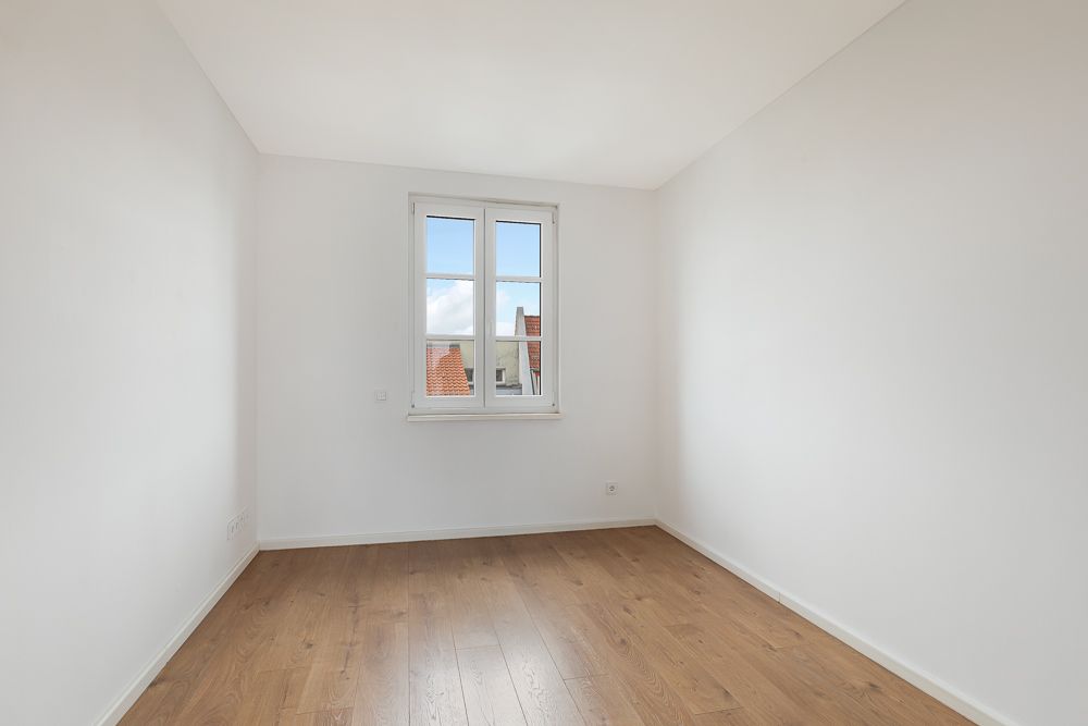 Leerer Raum mit weiß gestrichenen Wänden, Holzfußboden und einem Fenster.