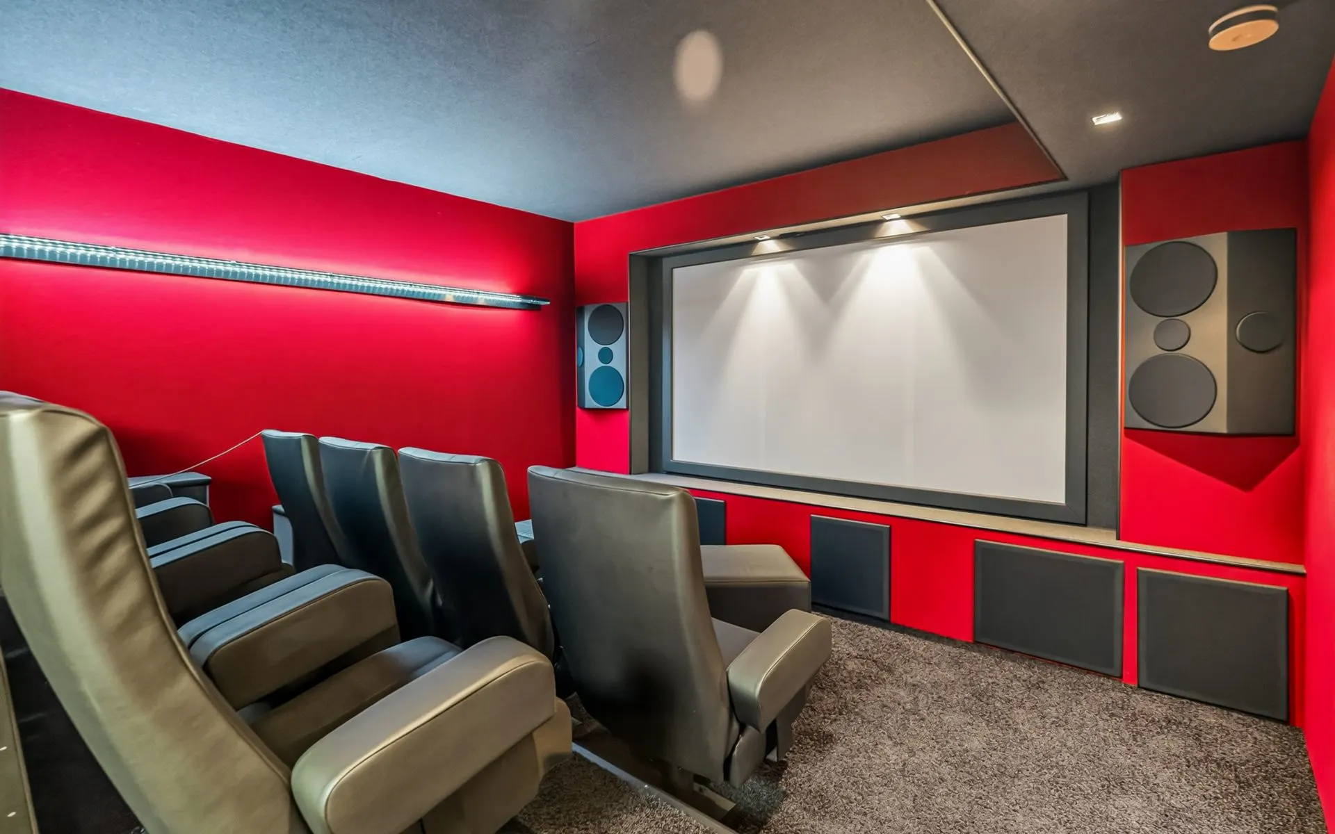 Heimkino mit roten Wänden, Leinwand, mehreren Ledersesseln und Lautsprechern.