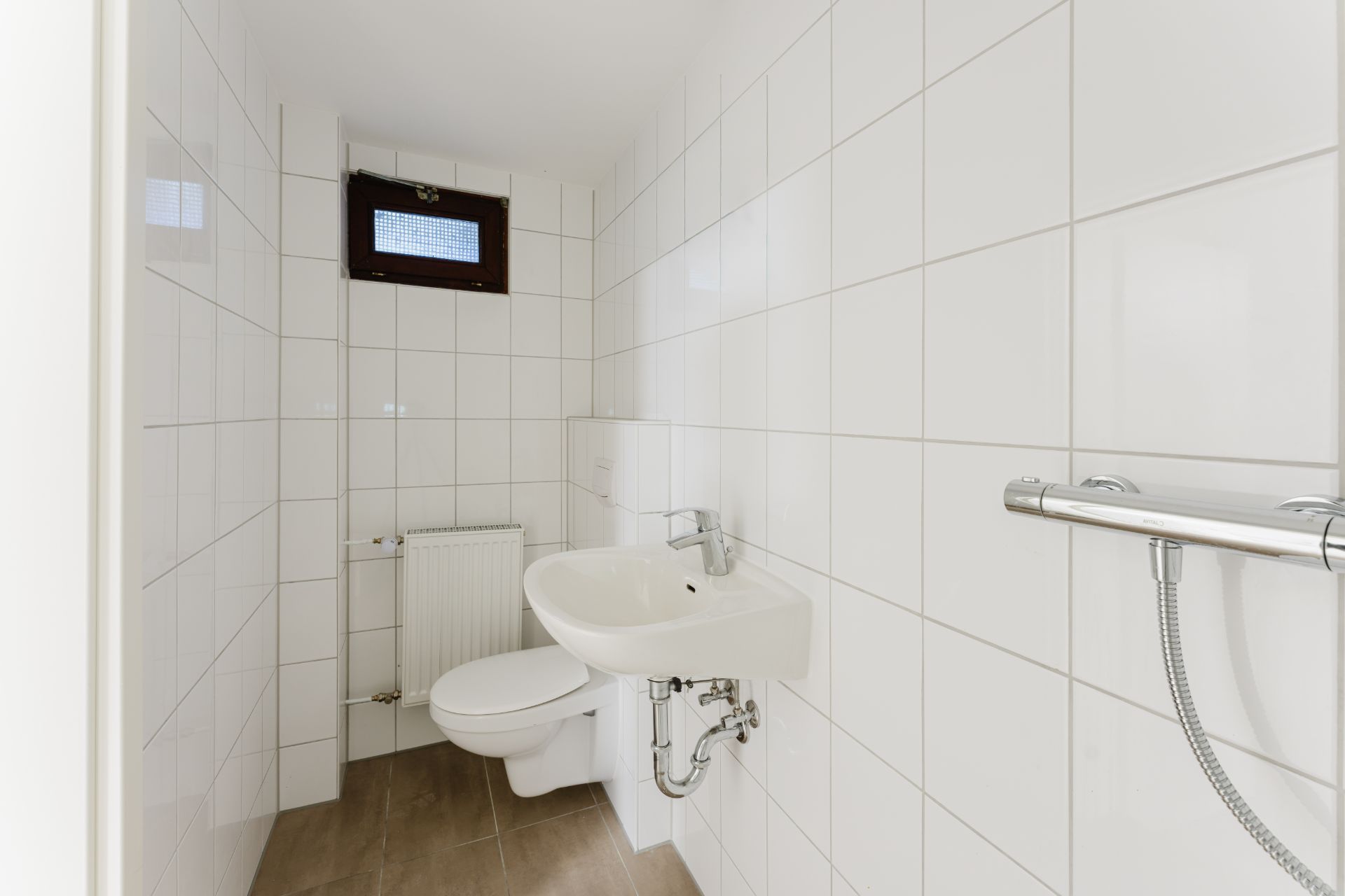 Kleines Badezimmer mit weiß gefliesten Wänden, WC, Waschbecken und kleinem Fenster.