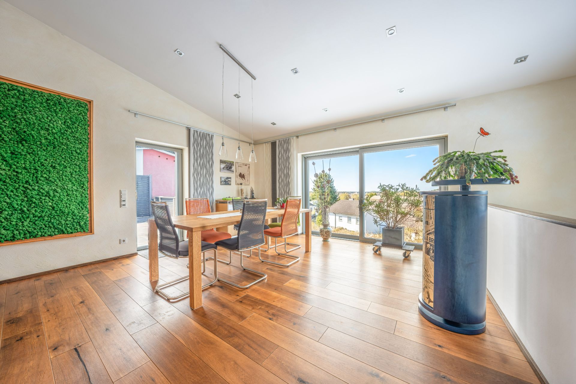 Heller Essbereich mit Holzboden, großem Fenster, Esstisch, Stühlen und Pflanzen.