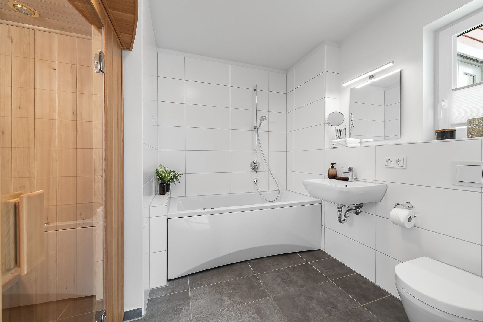 Modernes Badezimmer mit Badewanne, Dusche, Waschbecken, WC und angrenzender Sauna.