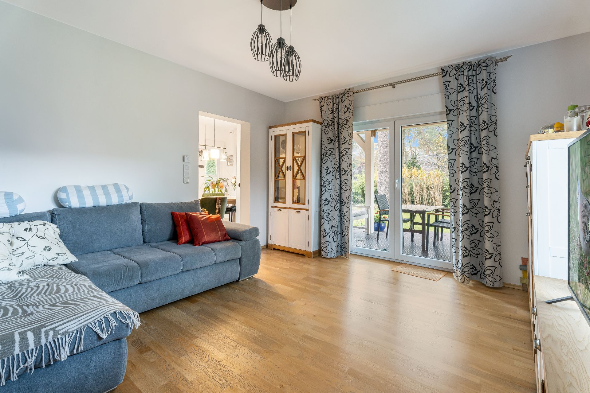 Wohnzimmer mit blauem Sofa, Holzboden, Glastür zur Terrasse und Schrank.