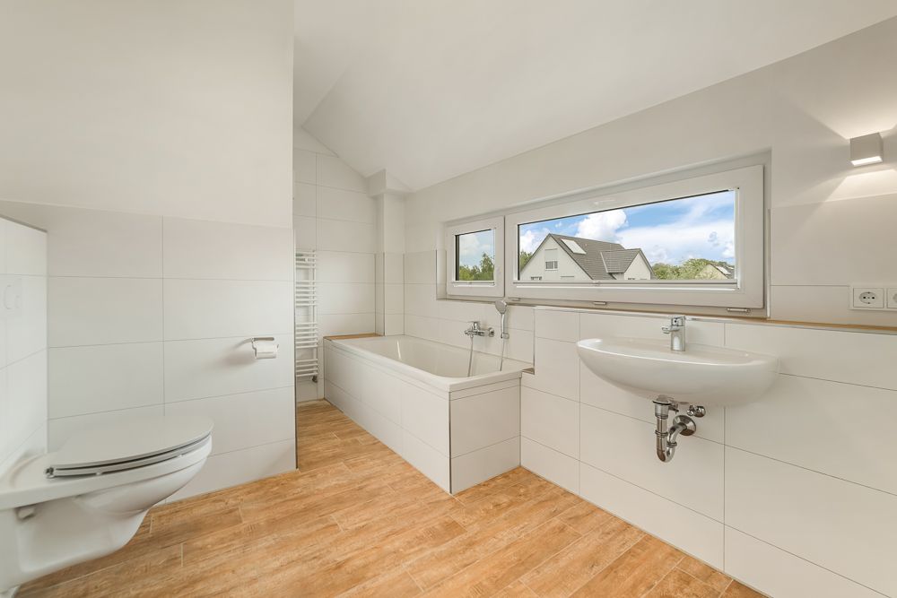 Helles Badezimmer mit Badewanne, Waschbecken, Wandtoilette und großem Fenster.