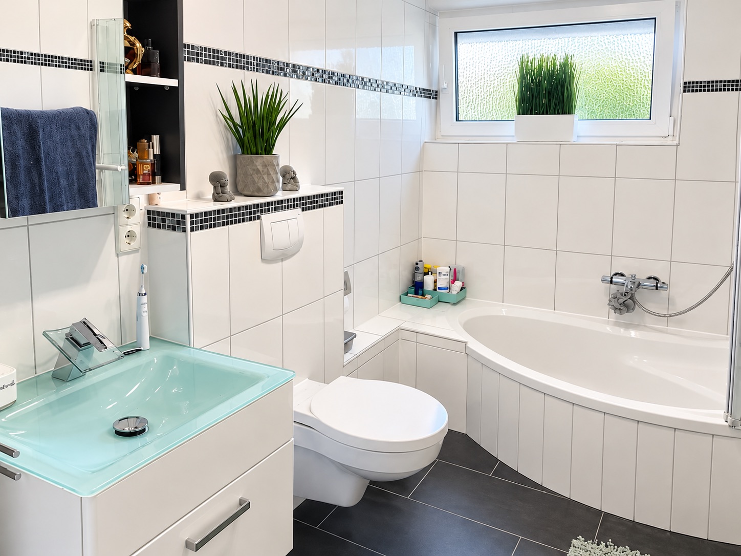 Modernes Badezimmer mit Eckbadewanne, Glaswaschbecken, Toilette und Fenster mit Pflanze.