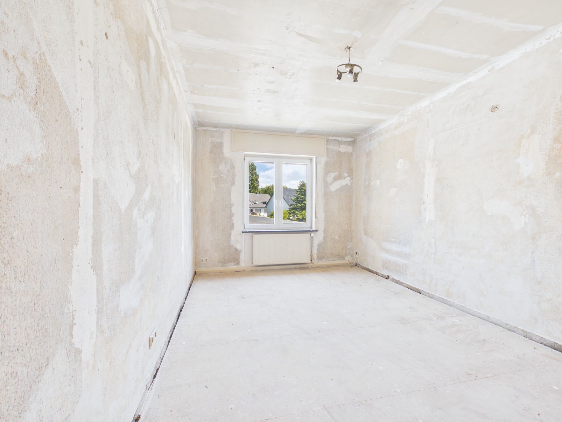 Leerer Raum mit verputzten Wänden, Fenster und Deckenleuchte, Boden ohne Belag.