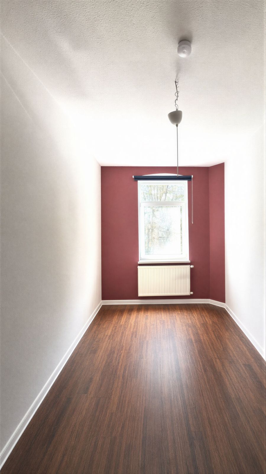 Schmaler, leerer Raum mit Holzfußboden, weißer Decke und Fenster an wand in bordeauxrot.