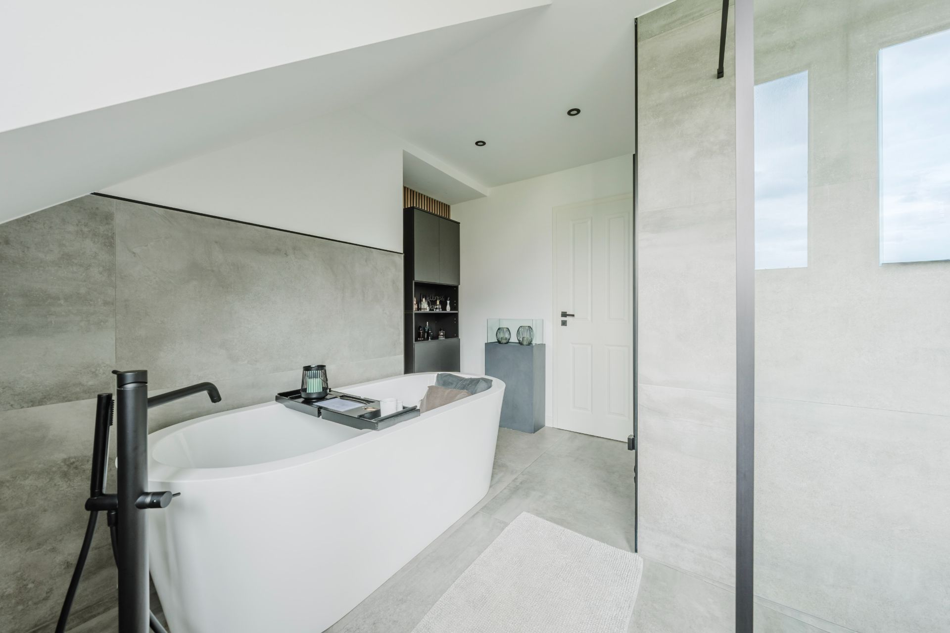 Modernes Badezimmer mit freistehender Badewanne, Glasduschwand und grauen Fliesen.
