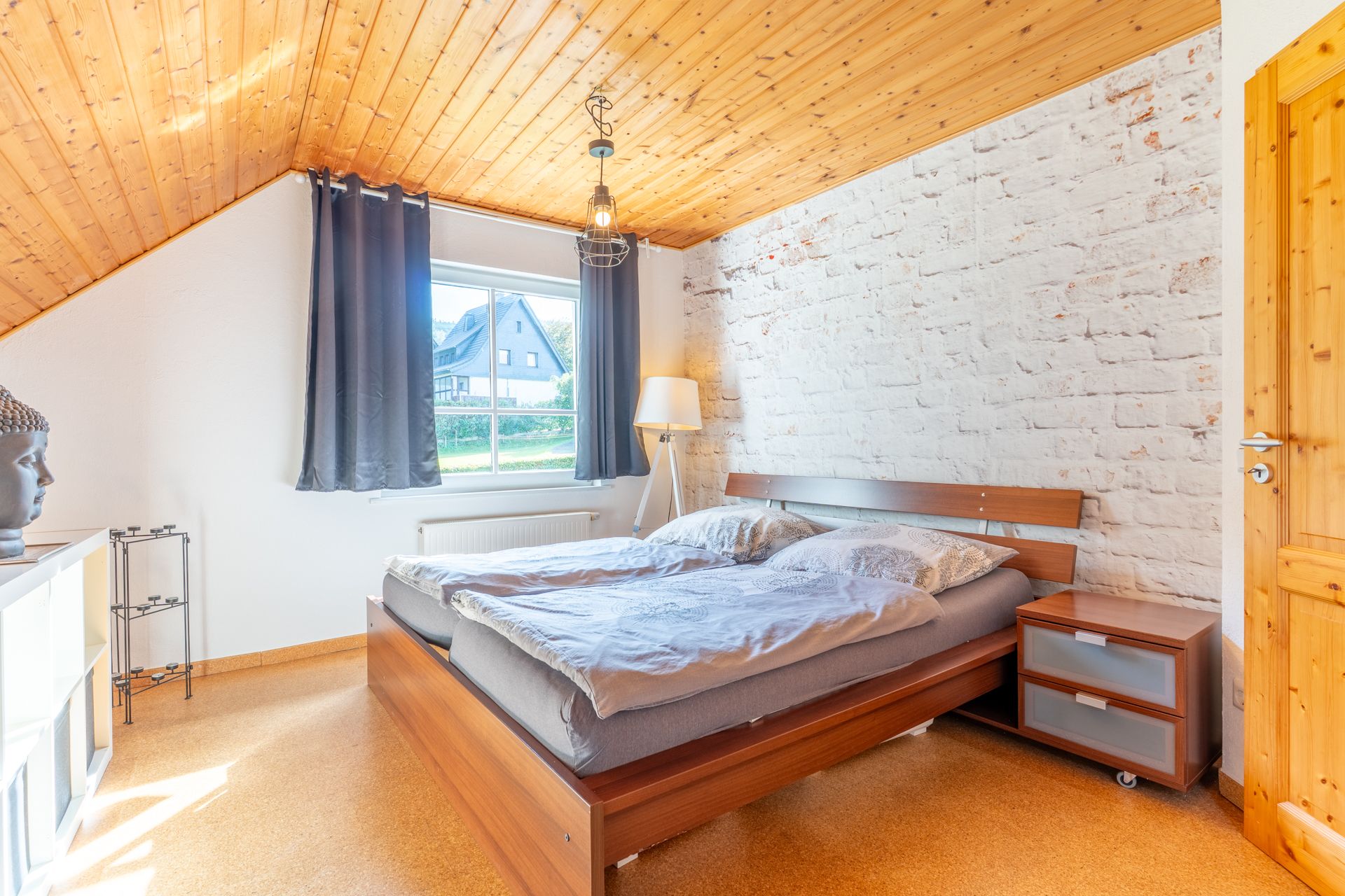 Helles Schlafzimmer mit Doppelbett, Nachttisch, Stehlampe und großem Fenster.