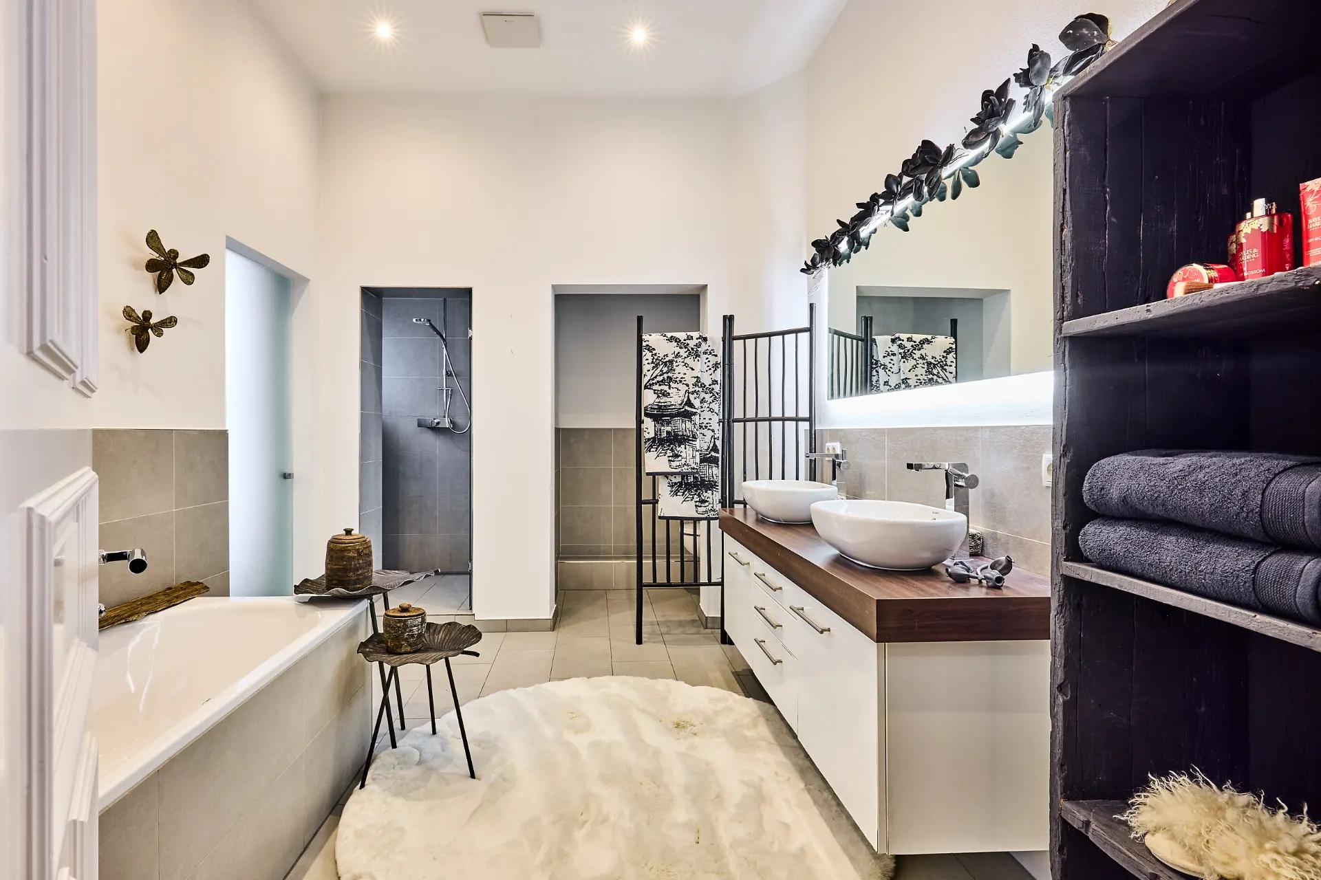 Modernes Badezimmer mit zwei Waschbecken, Badewanne, offener Dusche und Regal mit Handtüchern.