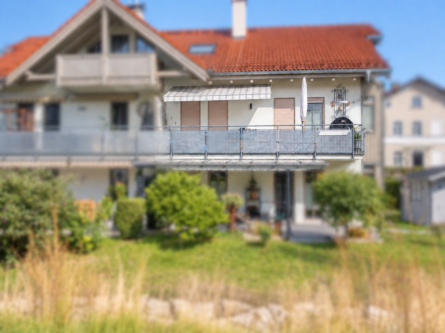 Doppelhaushälfte mit großem Balkon, roten Dachziegeln und Garten im Vordergrund.