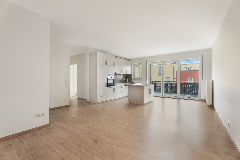 Helles Wohnzimmer mit offener Küche, Holzfußboden und großem Fenster mit Zugang zum Balkon.