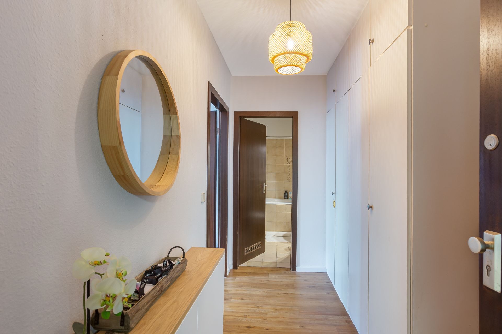 Heller Flur mit Holzfußboden, rundem Spiegel und Blick ins Badezimmer.