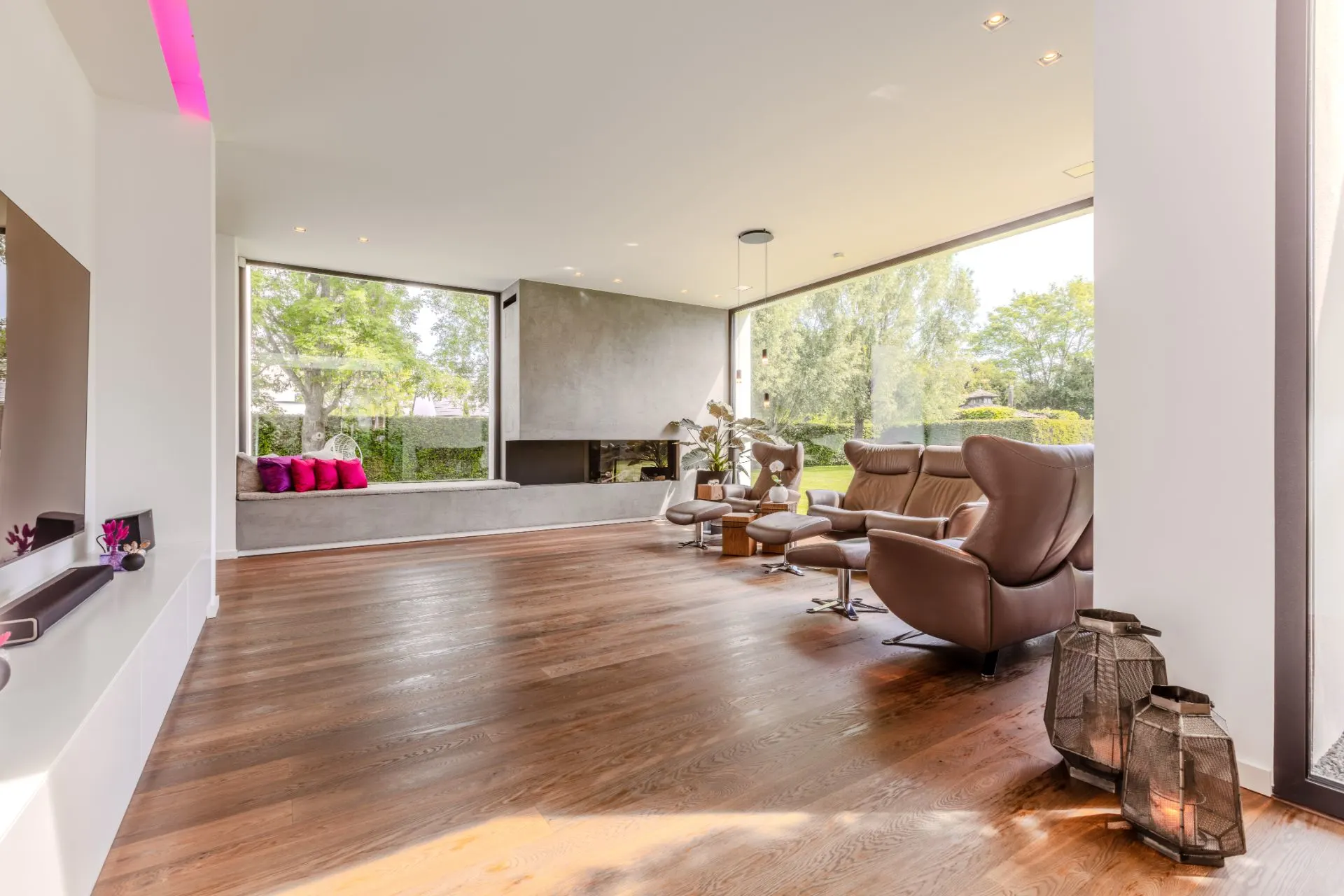 Modernes Wohnzimmer mit großen Fenstern, Holzfußboden und braunen Ledersesseln.