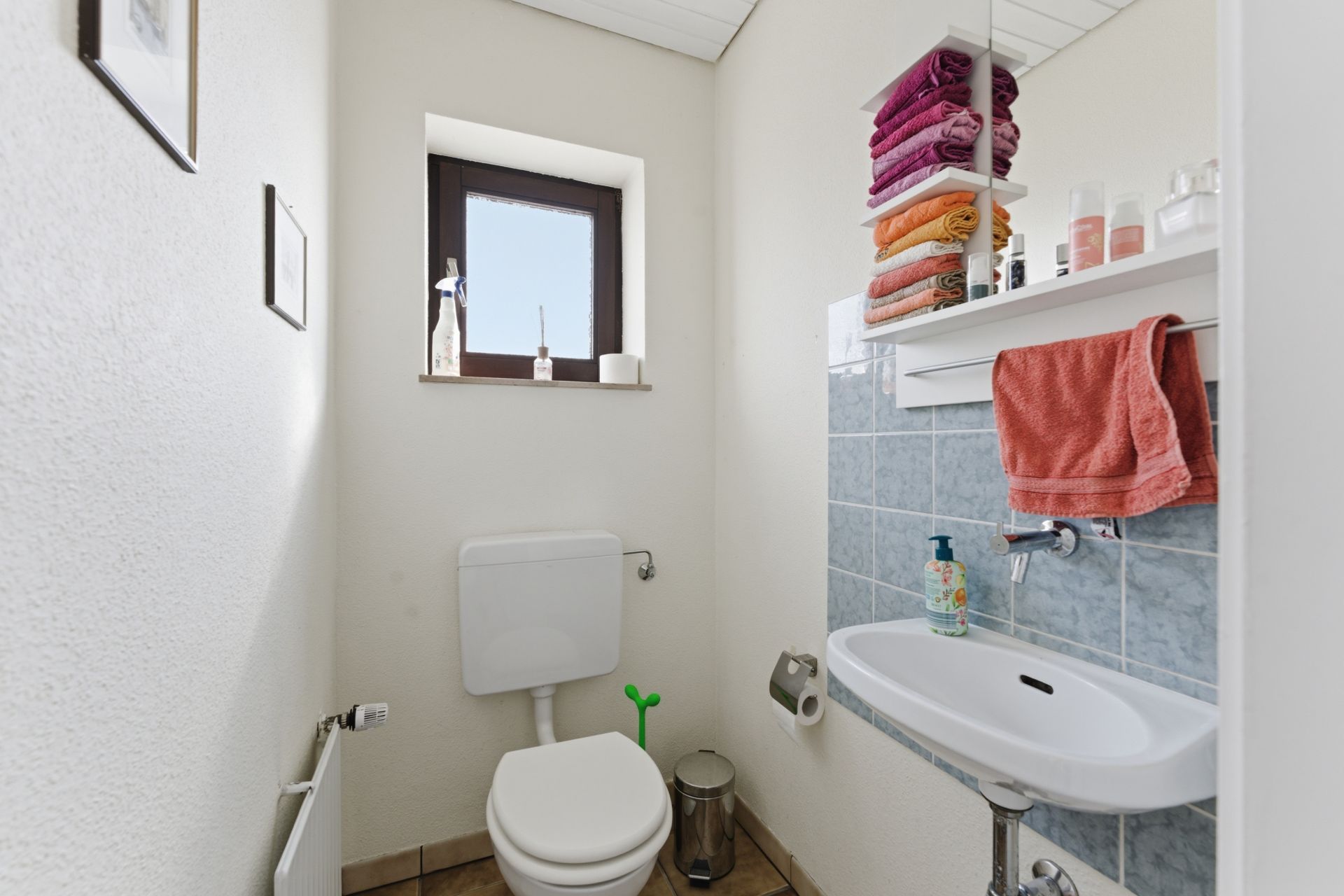 Kleines Badezimmer mit WC, Waschbecken, Regal, Handtüchern und Fenster.
