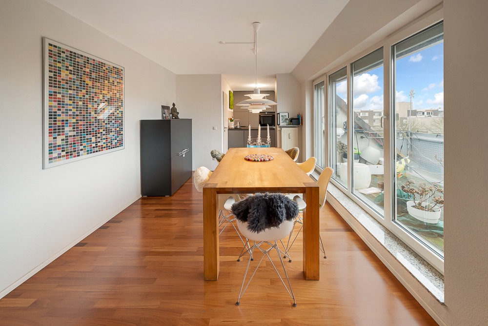 Esszimmer mit Holztisch, weißen Stühlen, großem Fenster und bunter Wandkunst.