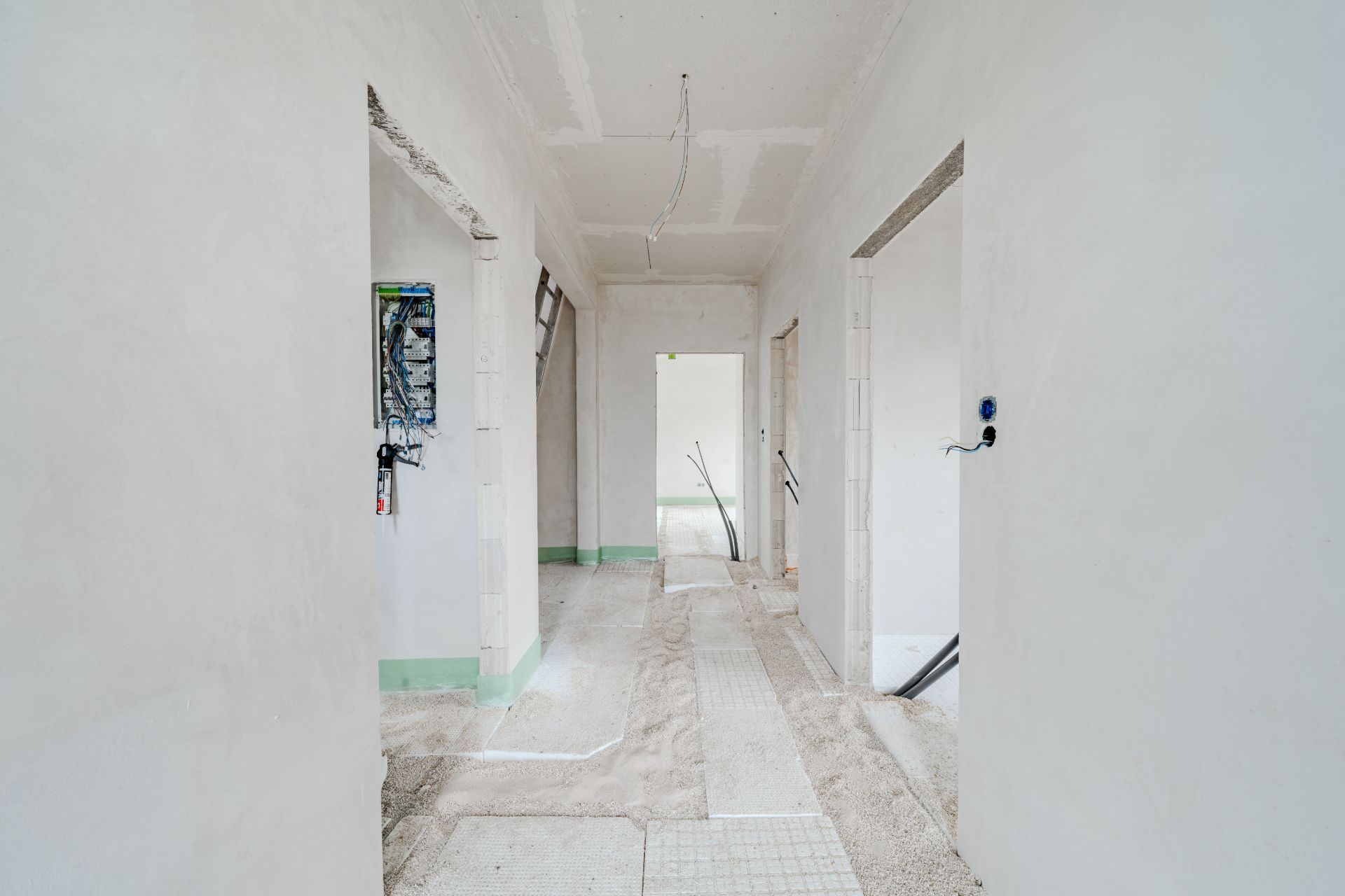 Heller Flur in einem Wohnhaus im Rohbau mit offenen Türrahmen und sichtbarer Verkabelung.