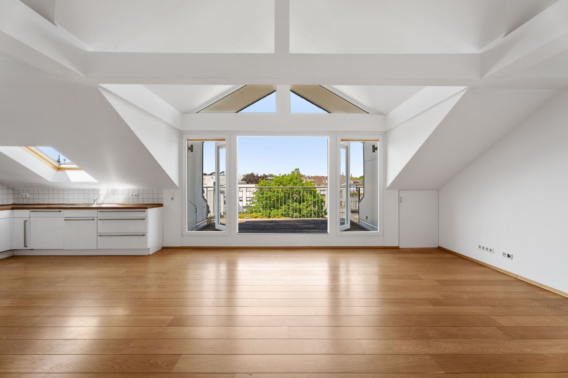 Helles Dachgeschosszimmer mit Holzfußboden, Einbauküche und Zugang zu einem Balkon.