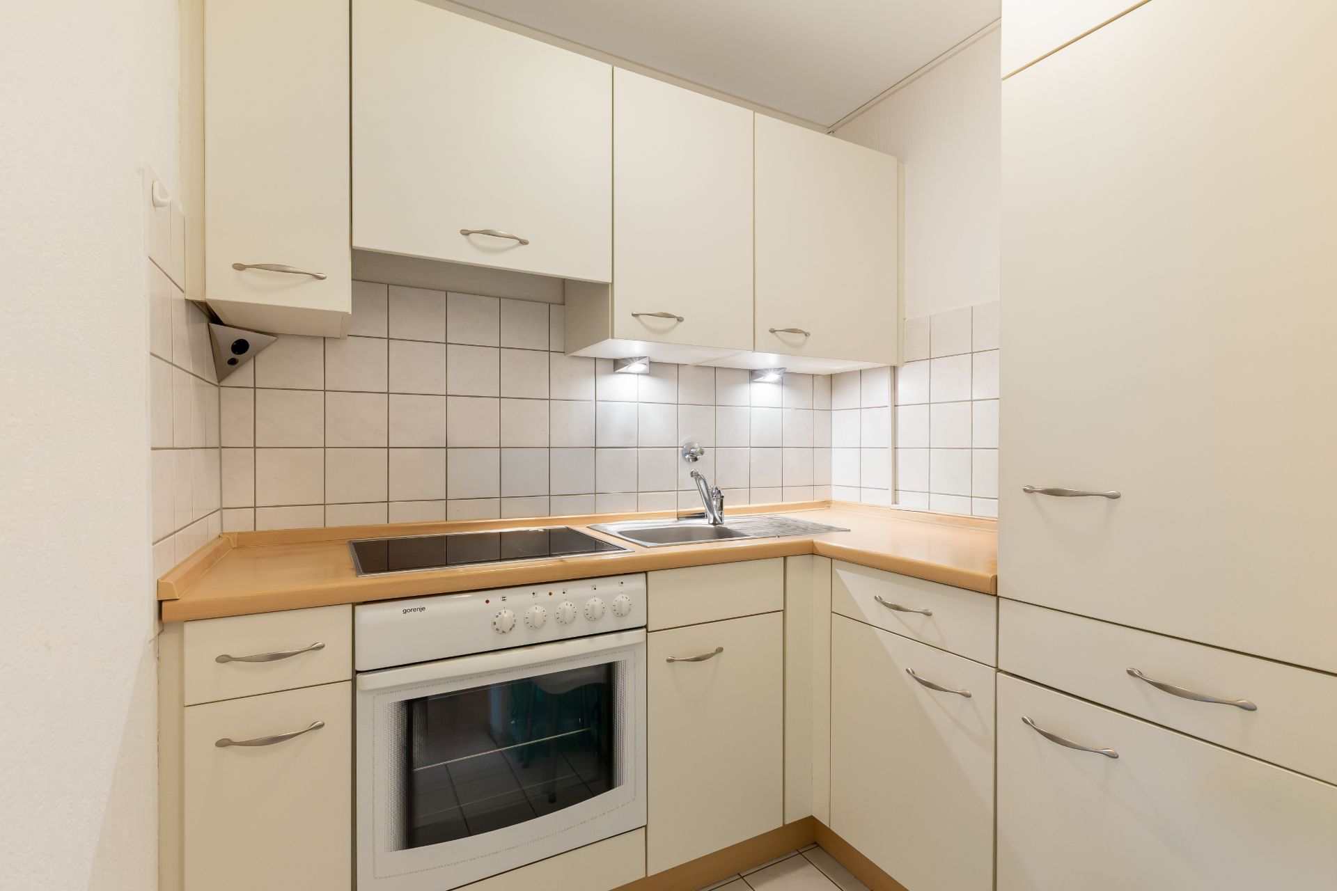 Kleine moderne Einbauküche mit Herd, Ofen, Spüle, weißen Schränken und Fliesenwand.
