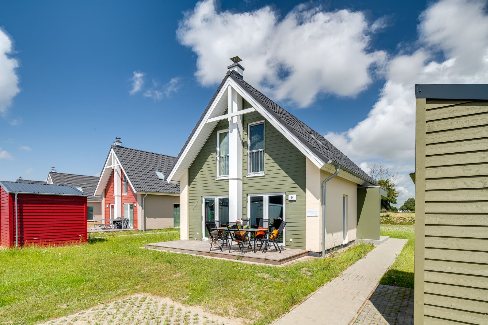 Modernes Haus mit grün-weißer Fassade, Terrasse und Gartenmöbeln auf einer Rasenfläche.